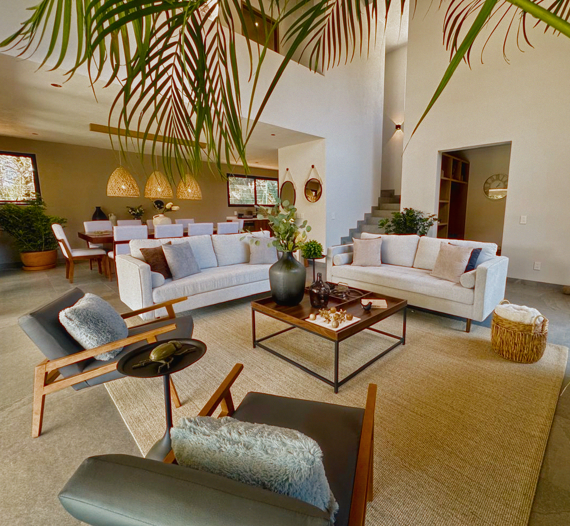 Sala de doble altura con palmas, sofás de lino y lámparas artesanales de mimbre